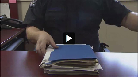 A police officer sitting at a desk with a pile of file folders in front of them