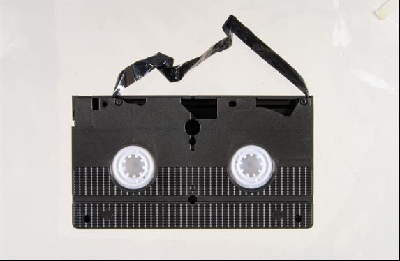 Vue du dessous d’une cassette VHS; un bout de ruban gravement plissé a été tiré hors de la cassette