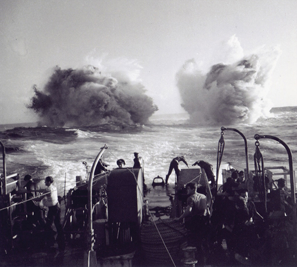 Two explosions are seen on the surface of the water from the perspective of a ship.