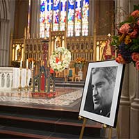 A framed portrait of John Turner is seen at the forefront, with a view of St. Michael’s Cathedral Basilica’s altar in the background.