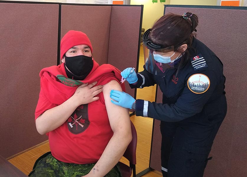 Le caporal-chef Sinclair Childforever de Fort Severn reçoit un vaccin contre la COVID-19 alors qu’il aide les techniciens paramédicaux à vacciner les résidents de Sachigo Lake. Photo : M 2 Kevin McCue. ©2021 DND/MDN Canada