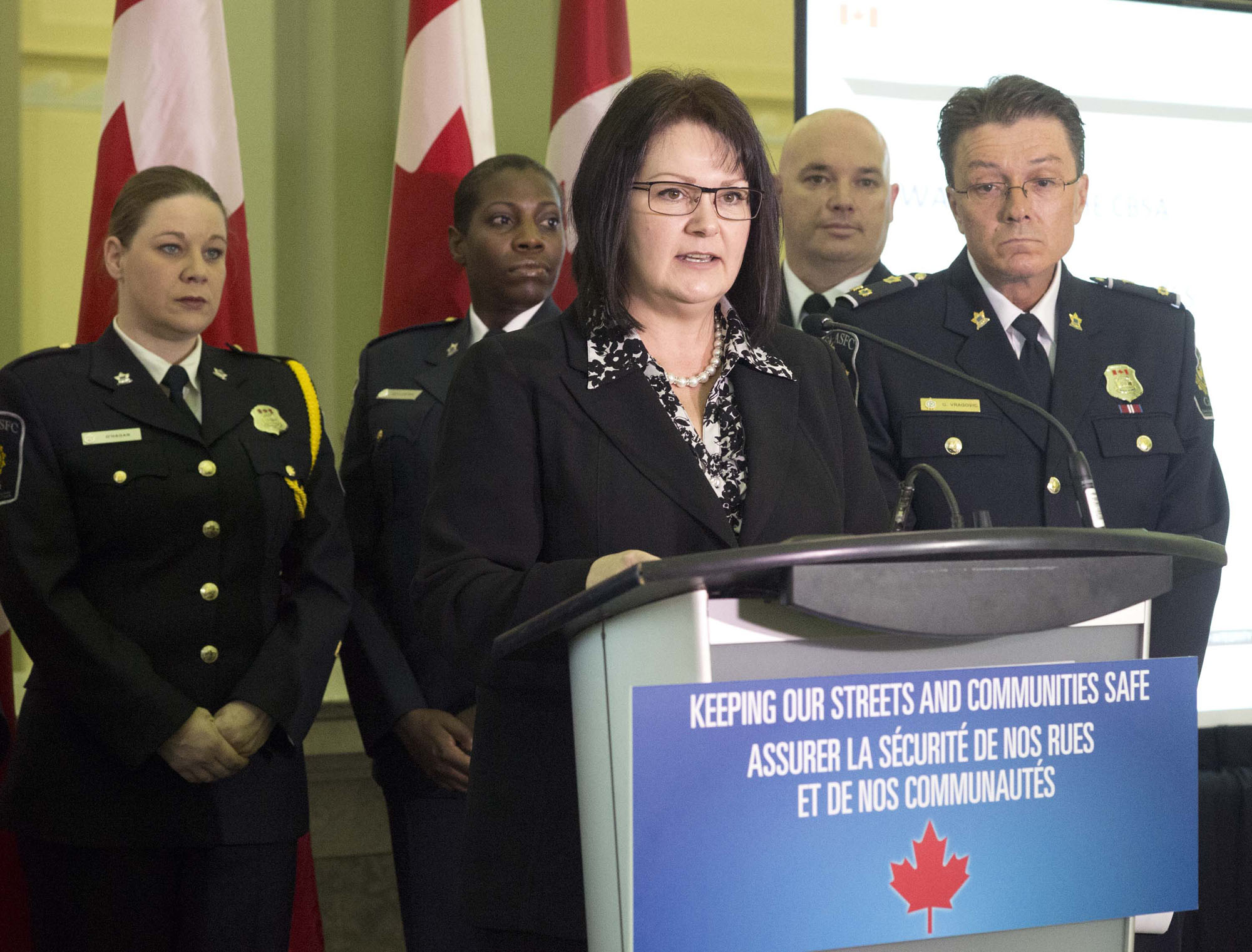 Roxanne James, Parliamentary Secretary to the Minister of Public Safety and Emergency Preparedness, and Goran Vragovic, Canada Border Services Agency (CBSA) Regional Director General for the Greater Toronto Area, announce additions to the "Wanted by the CBSA list" as the CBSA Honour Guard looks on.
