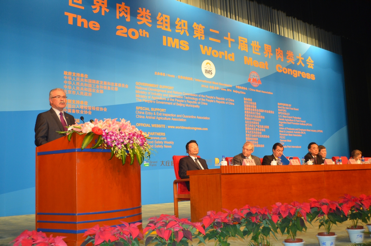 Minister Ritz standing behind podium decorated with a bouquet of bright flowers as he speaks in front of delegates at the World Meat Congress in Beijing.