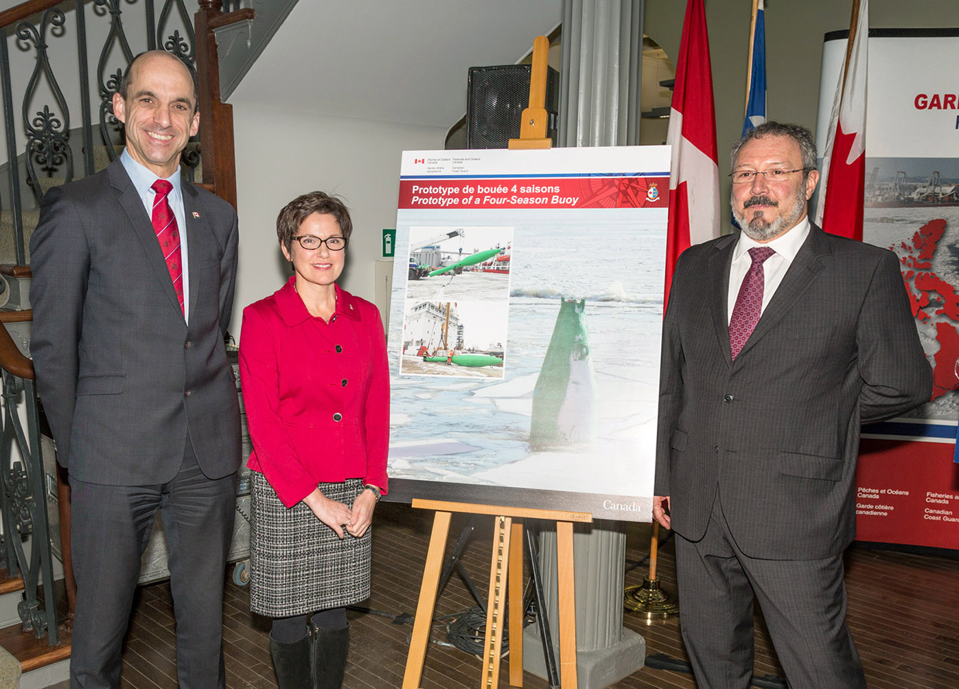 The Honourable Steven Blaney, Minister of Public Safety and Emergency Preparedness Canada, Sylvie Pelletier, Director of Programs at the Canadian Coast Guard, and Jean-François Belzile, Director of Marine Operations, Shipping Federation of Canada, pose in front of images of a prototype of new generation four season buoys that will be deployed by the Canadian Coast Guard between Québec and Montréal over the next few years.