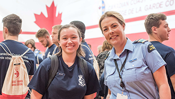 A Canadian Coast Guard Academy officer cadet and an instructor smile at the camera during an indoor event.
