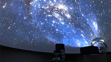Planetarium dome displaying a starry night sky with projectors and equipment visible at the bottom.