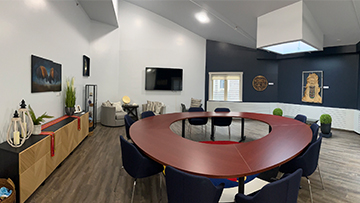 A meeting room with a large, circular wooden table surrounded by chairs, Indigenous art and a flat-screen TV.