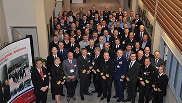 A large group pose for a photo in a hallway wearing uniforms and suits.