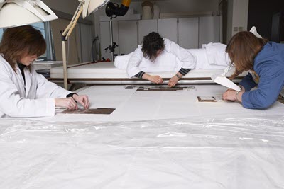 Three women in lab coats working on the flag.