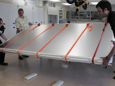 Three men turning over the flag, packaged and placed between two metal boards secured with five straps.