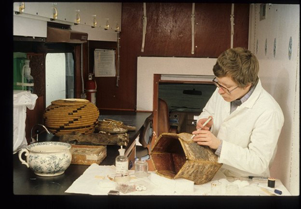 A conservator working inside the mobile lab uses a syringe to stabilize the seam of a basket.