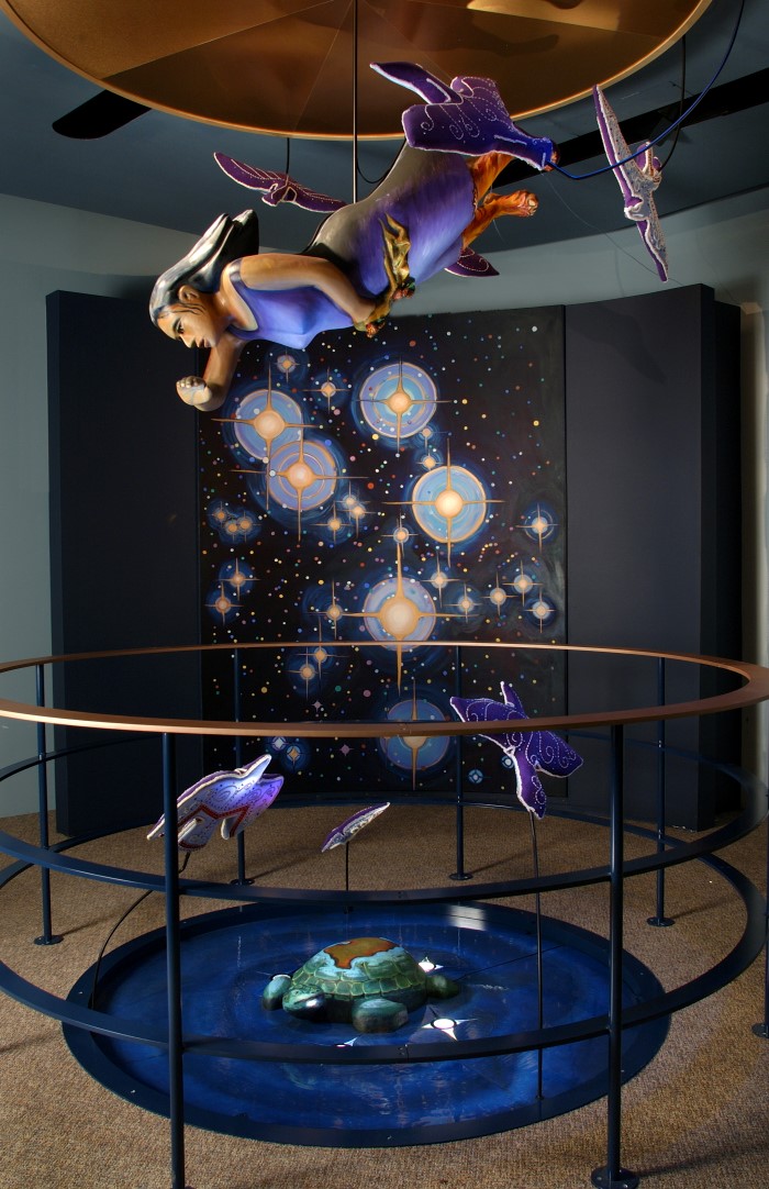A sculpture of a woman is suspended above representations of the stars, different animals and the Earth floating in the universe.