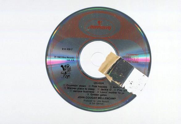 Audio CD viewed from the label side with a portion of the label and metal layer of the disc peeled away because of the removal of an adhesive label