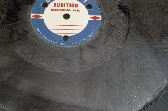 A grooved acetate record disc showing a white waxy deposit on the surface