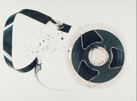 A reel of VHS tape that has been removed from the cassette housing with some tape unwound and showing flakes coming off the tape base