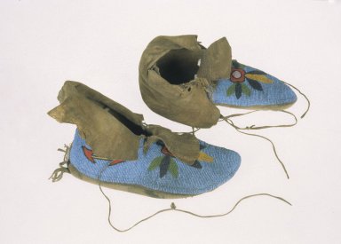 Mocassins abondamment ornés de perles de verre, créant des motifs de fleurs avec en arrière-plan des perles bleu pale.