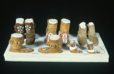 Five pairs of moccasins in different sizes, from a small pair for children to adult-sized, sitting on foam and padded with fabric-lined inner foam supports.
