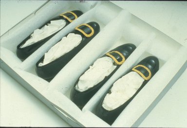 Two pairs of black shoes with gold buckles, padded out with tissue paper and placed within individual rectangular slots made out of foam inside the same box.