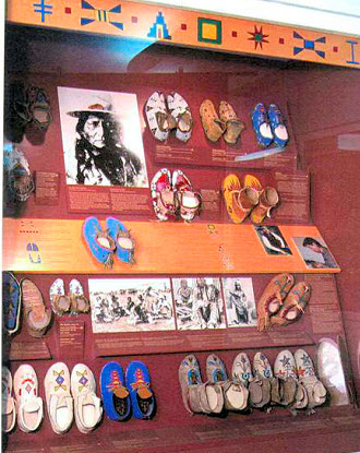 A large display case with many pairs of moccasins and a series of photographs.