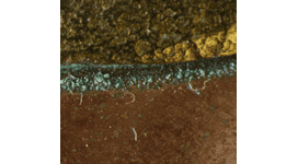 A close up of green copper corrosion, on a copper pot, located in the join where the brass handle joins the pot.