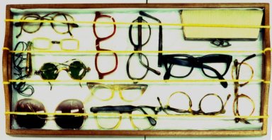 Quatre cordelettes tendues au-dessus d'une collection mixte comprenant des lunettes, un sac à main et un éventail rangés sur un plateau.