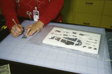 A conservator punctures the Ageless Eye indicator packet with a pen knife. The prepared pouch rests on the table beside her.