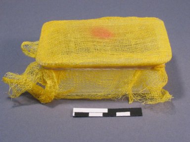 A side view of an object stored in a box covered in muslin. A red discolouration is visible on the muslin.