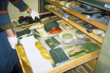 A shallow drawer is opened to reveal a variety of objects, such as twine, tools and pouches.