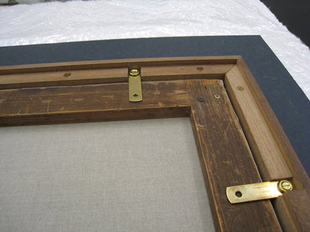 : A photograph of the back of a framed painting. The painting is flush with the extension, and straight mending plates hold it in place.