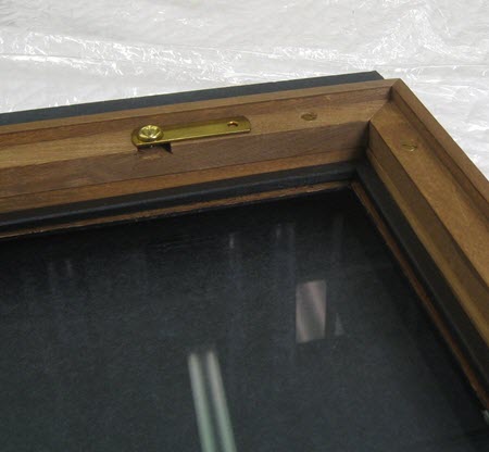 Photograph of a back corner of a frame with glazing. Padded, black wood spacer strips are attached to the inside perimeter of the glazing.
