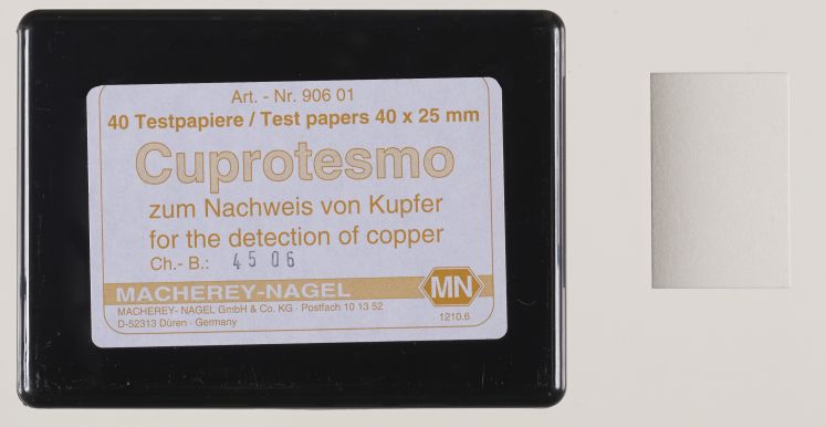 La boîte est étiquetée : Test papers 40 by 25 mm, Cuprotesmo for the detection of copper, Macherey-Nagel. Le papier réactif est un rectangle blanc.