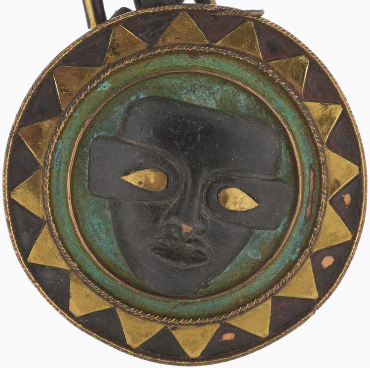 The pendant is circular with a dark gray face in the centre enclosed by two metal rings. The eyes of the face are yellow, and there are yellow triangles between the outer circle and the edge of the pendant.