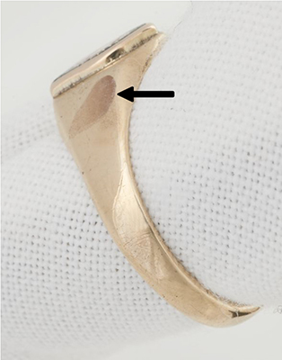 Corrosion spot on a yellow gold ring after electrolysis indicated by an arrow