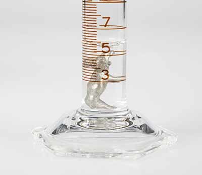 Small metallic object after immersing in water in a 25 mL graduated cylinder. The level of the water is about 0.6 mL more than before the object was immersed.