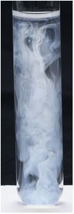 The liquid in the test tube is full of white swirls, standing out against the black background.