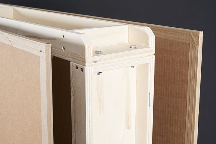 Corner detail showing assembly hardware and triwall cardboard covers with reinforced kraft paper tape on the edges