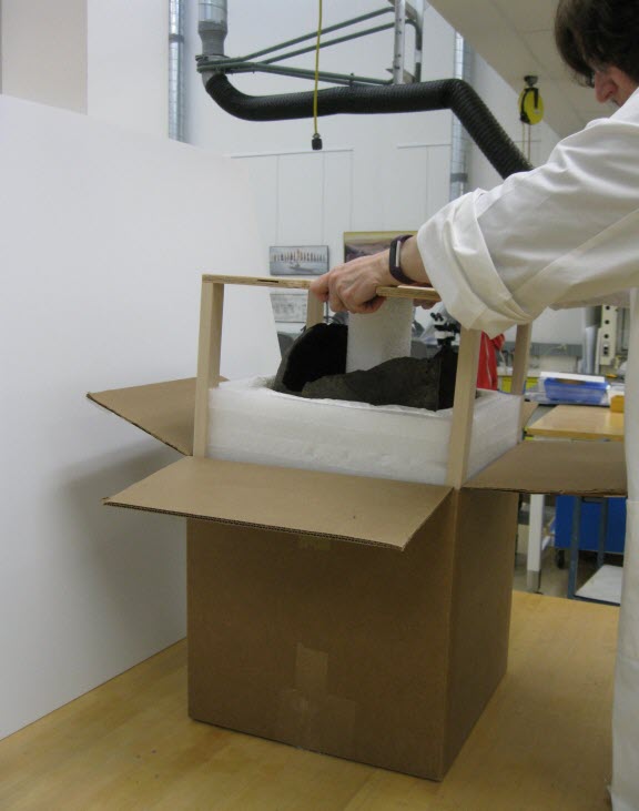 A conservator inserting the ceramic vessel and mount assembly into an interior corrugated box.