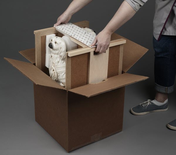 A person inserts a restraint system containing two dog sculptures into a box.