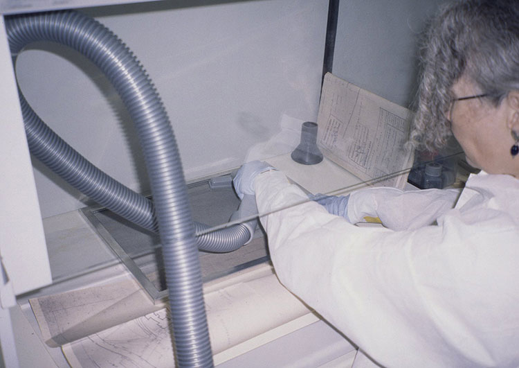 Conservator working at a class 1 biological safety enclosure and using a vacuum cleaner nozzle to remove mould from a document