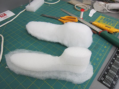 De la bourre ouatée de polyester est enroulée autour d’une forme en mousse de polyéthylène sculptée afin de constituer une surface matelassée souple qui servira de support interne pour des chaussures.