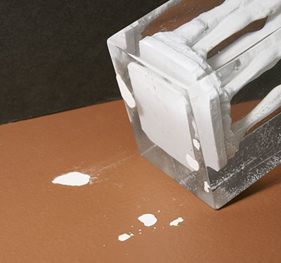 Fragments of paint are strongly adhered to an acrylic object removed from a painted dark brown surface.