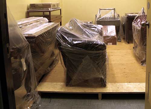 Pièces de mobilier enveloppées dans une pellicule de polyéthylène et entreposées à 10 cm du sol sur un faux-plancher en bois.