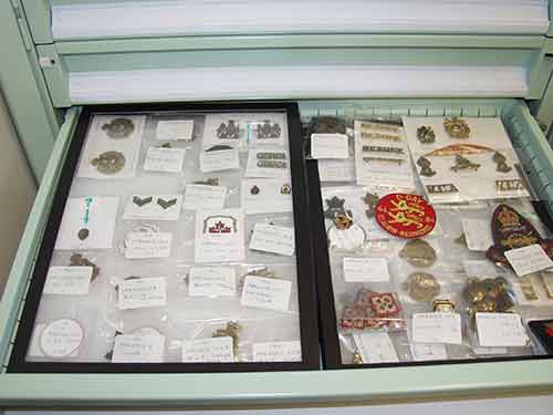 An open drawer in a metal filing cabinet contains many small objects such as military insignia in small transparent bags.