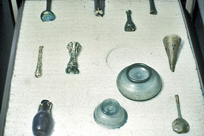 Objets archéologiques en verre, dont certains présentent une surface endommagée, sur un tiroir de rangement matelassé.