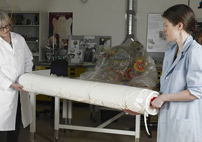 A flat flexible object rolled on a padded tube being transported by two persons.