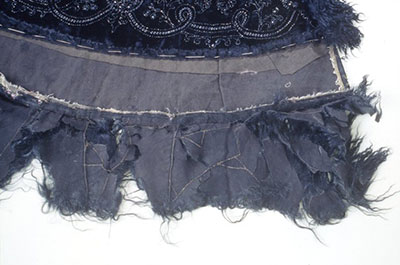 Detail of damages to the black fur trim on a black velvet cape.