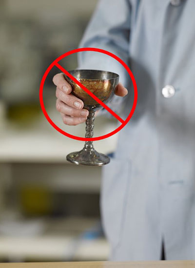 A tarnished silver-plated goblet being handled without gloves. A red circle with a diagonal line running through it covers most of the image and indicates that this is not appropriate.