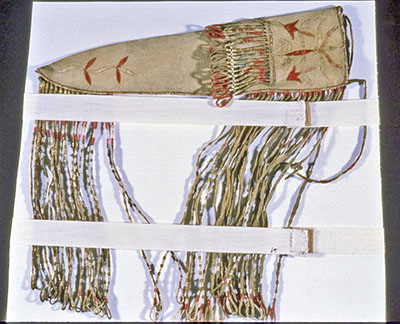 Étui à couteau avec de longues franges décorées de piquants de porc-épic, posé sur un support de rangement qui protège les franges.