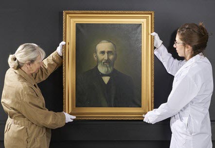 Two people handling a medium-sized painting.