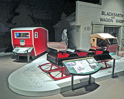 Two sleighs are exhibited on a raised platform which is also used as a display aid suggesting snow.
